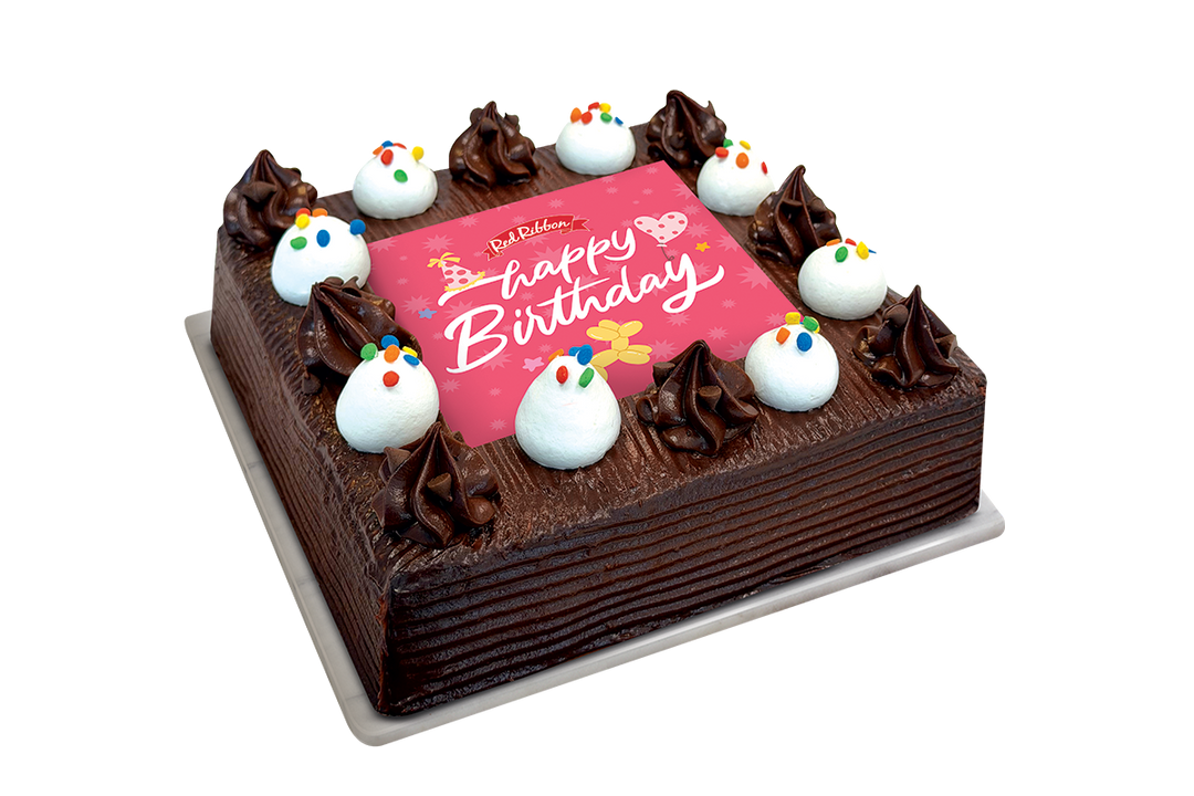 A square chocolate cake with dark chocolate frosting, decorated with piped chocolate swirls, white frosting dollops with colorful sprinkles, and a pink 'Happy Birthday' plaque on top, shown on a white background.