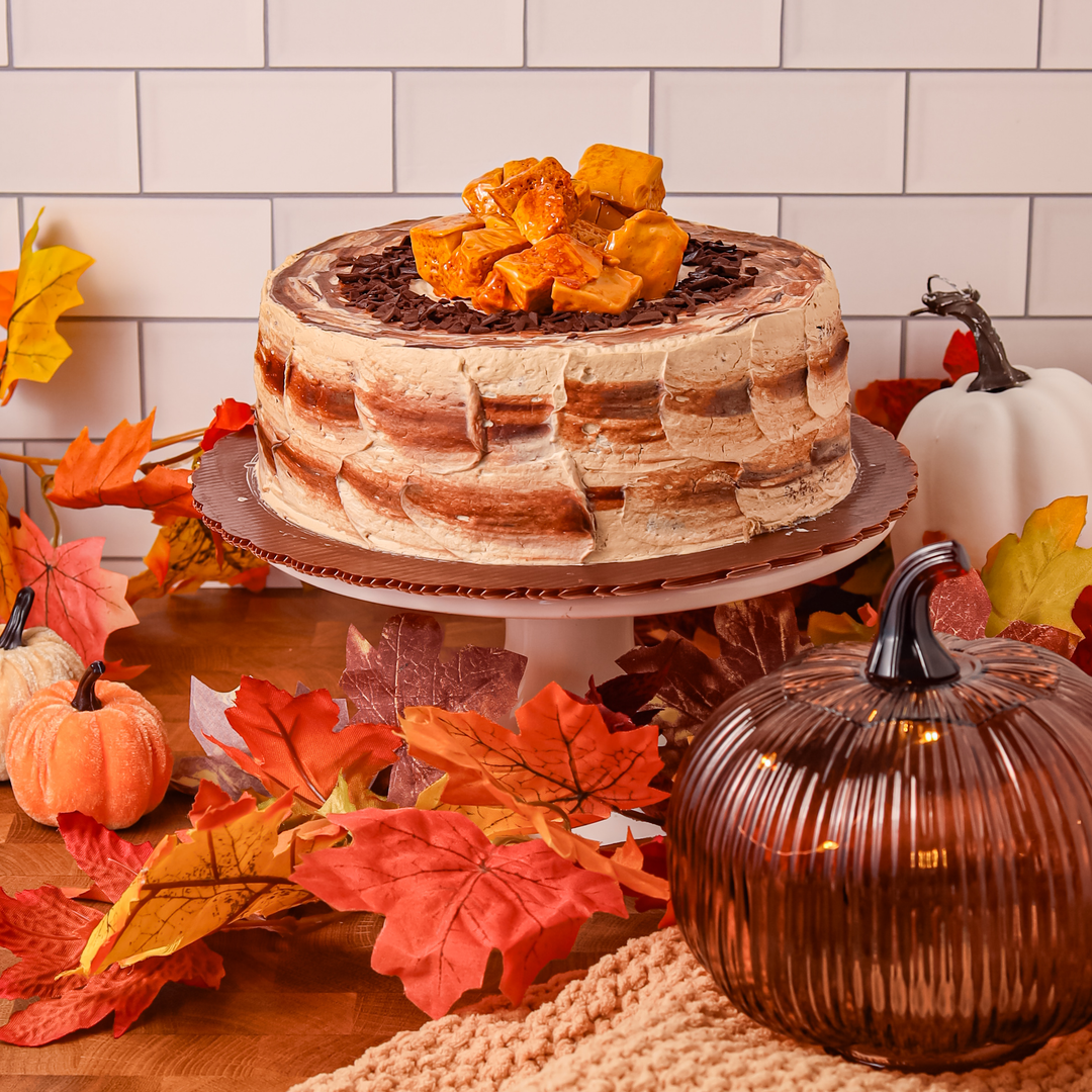 Red Ribbon Choco Mocha Crunch Cake on a cake stand with autumn decorations, pumpkins and maple fall leaves