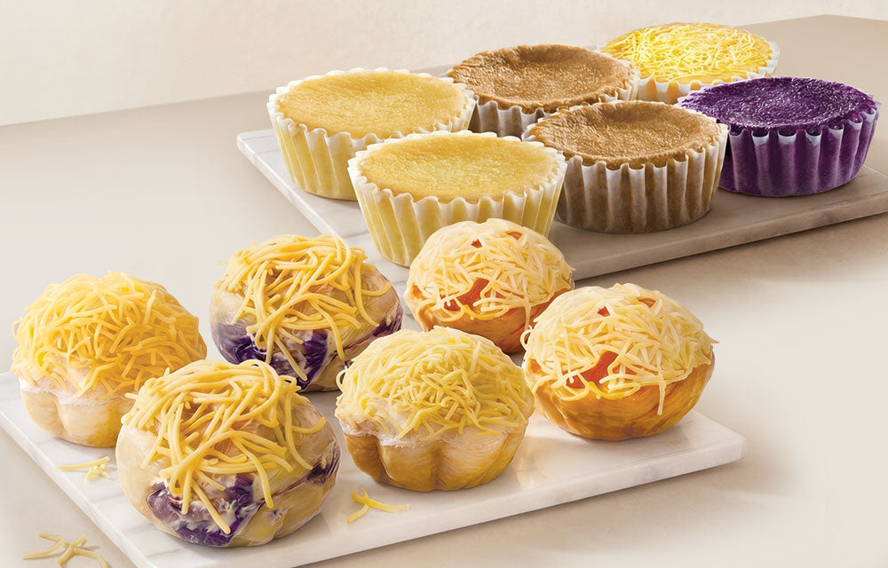Assorted mamons and ensaimadas with different colored cheese toppings  on a white surface