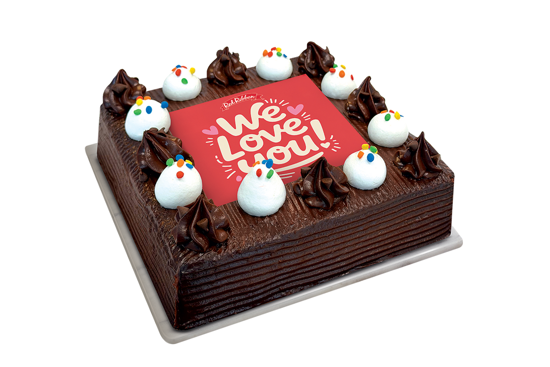 A square chocolate cake with piped dark chocolate frosting, decorated with white frosting dollops and colorful sprinkles, featuring a red top panel with the words 'We Love You!' in white script.