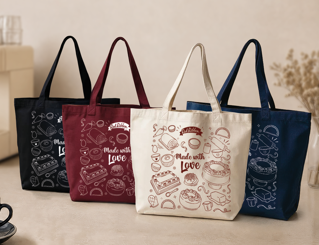 Four canvas tote bags with handles are lined up on a tabletop against a warm beige background. The bags are in black, burgundy, cream, and navy, each printed with food illustrations and the words 'Made with Love'.
