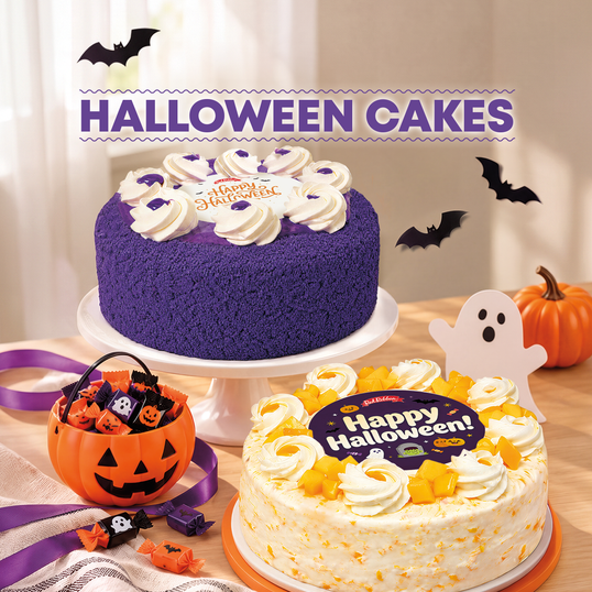 Red Ribbon Halloween Cakes featuring a vibrant purple Ube Overload cake and a Mango Supreme cake topped with festive "Happy Halloween!" edible toppers, whipped cream swirls, and Halloween decorations like bat silhouettes, a pumpkin bucket, and a cute ghost cutout