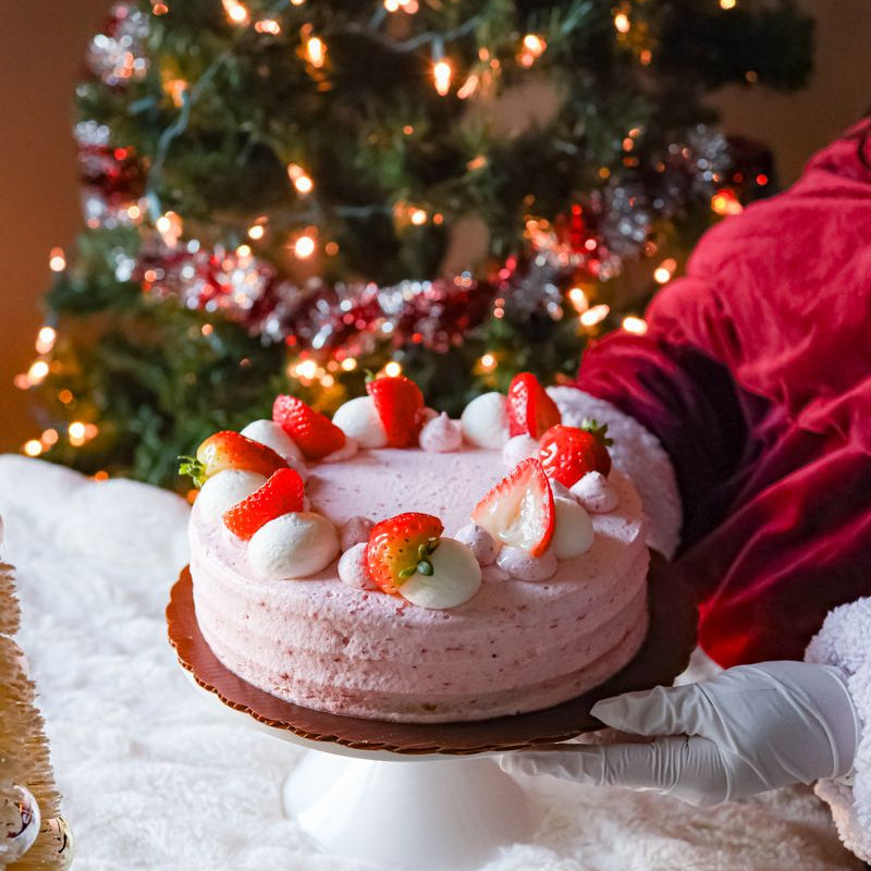Strawberry Dream cake with strawberries on a stand in front of a decorated Christmas tree.