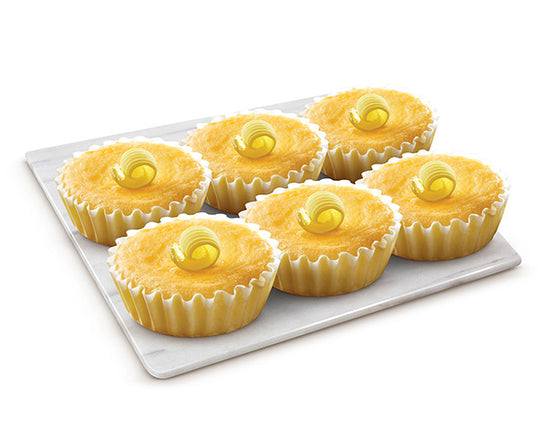A pack of six butter mamons on a white plate with a curl of butter topping each mamon on a white rectangular plate.
